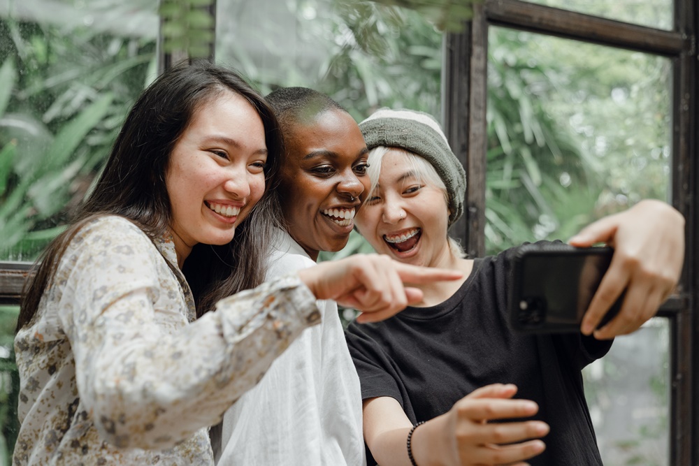 Três mulheres apontando para um celular e sorrindo