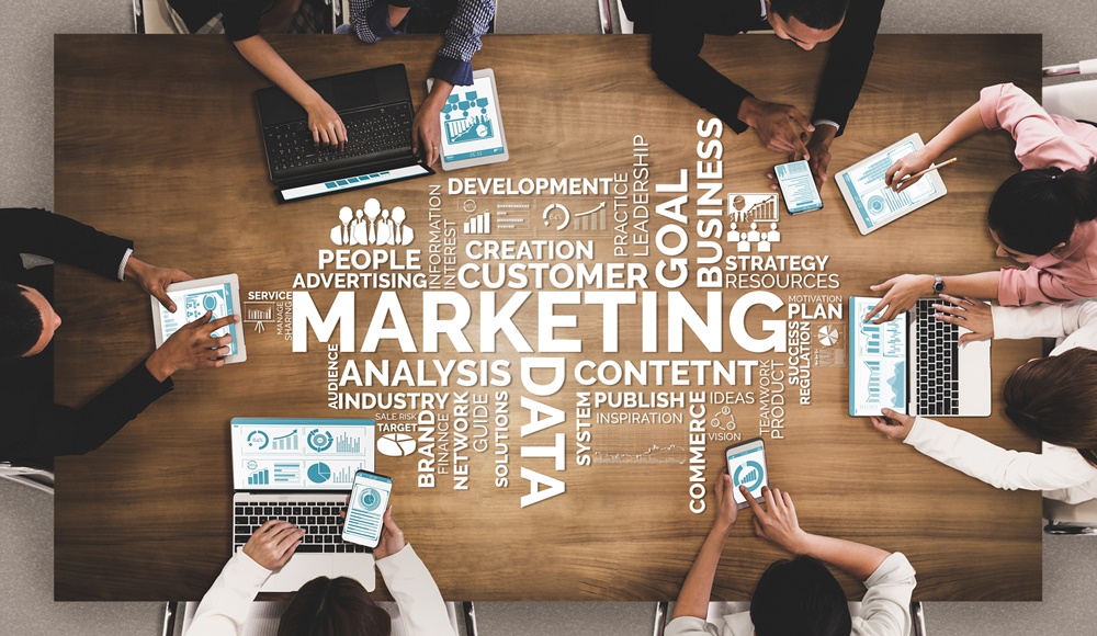 imagem aérea de pessoas sentadas em uma mesa e palavras relacionadas a marketing digital dispostos no centro.